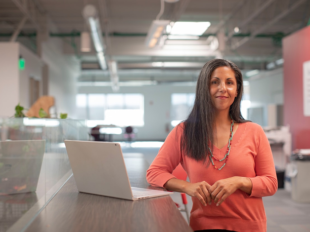 Woman in orange shirt sitting beside table with laptop